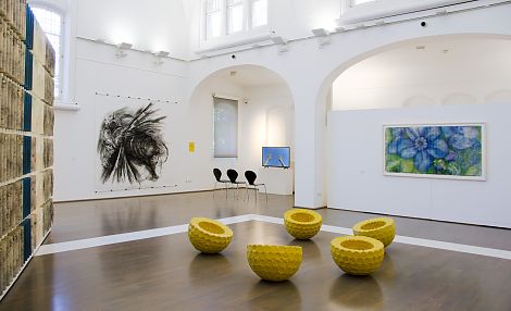 <h1>Kunstmuseum Heidenheim</h1><p>Hinterer Bereich des großen Ausstellungssaales mit Videoinstallation, Bienoptik-Kaukasisches Veilchen und der Zeichnung Flug 3. Auf dem Boden die Gruppierung Soziales Prinzip 1.</p>